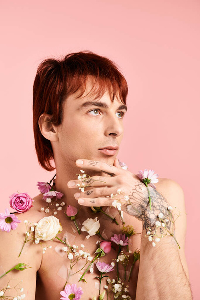 A shirtless young man strikes a pose with colorful flowers spread across his chest, set against a pink studio background. - Photo, Image
