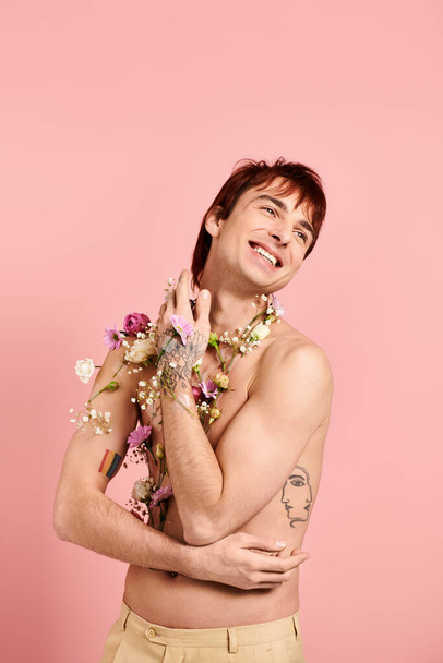 Un joven, sin camisa, orgullosamente mostrando flores en su pecho en un estudio con un fondo rosa. - Foto, imagen