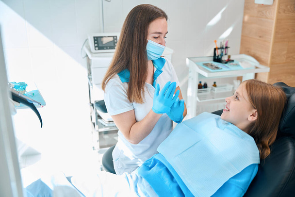 Adolescent dans une chaise dentaire à une réception d'une orthodontiste, un médecin dans un masque de protection et des gants - Photo, image