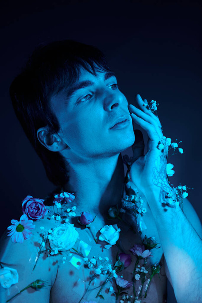 Un giovane circondato da fiori in uno studio con luce blu - Foto, immagini