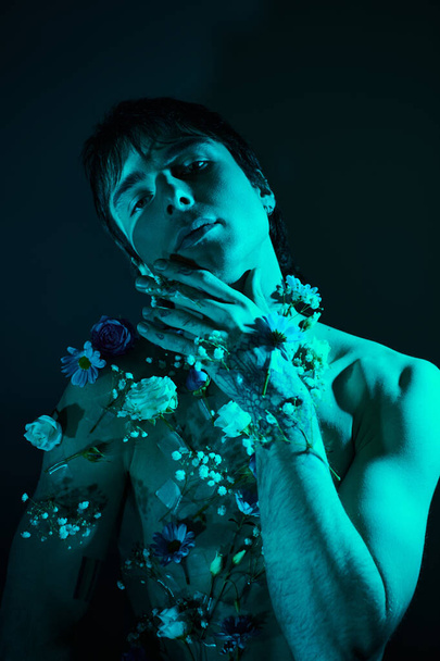 A young man stands shirtless with a garland of flowers around his neck in a studio - Photo, Image