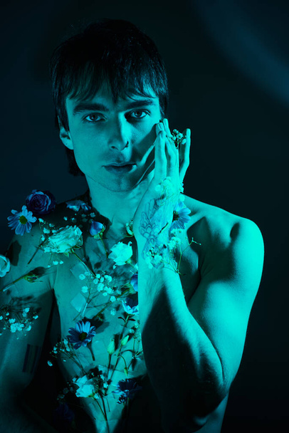 Молодий чоловік з квітами на грудях тримає руки на обличчі в споглядальному жесті. - Фото, зображення