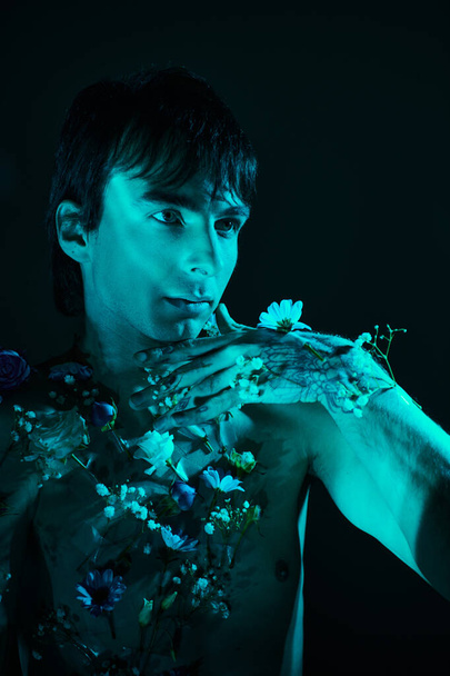 Hombre sin camisa rodeado de flores posando en el estudio con luz azul - Foto, imagen