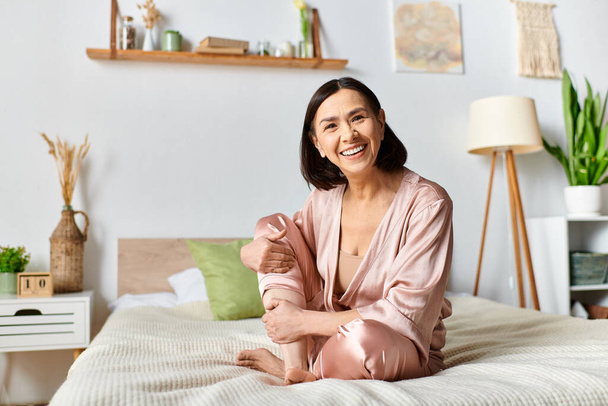 Une femme mûre dans des vêtements de maison confortables se trouve au sommet d'un lit, souriant contentement. - Photo, image