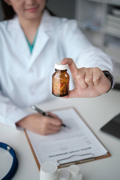 Junge schöne asiatische Ärztin mit Tabletten Flasche Schrift auf Dokument in der Klinik. Hochwertiges Foto - Foto, Bild