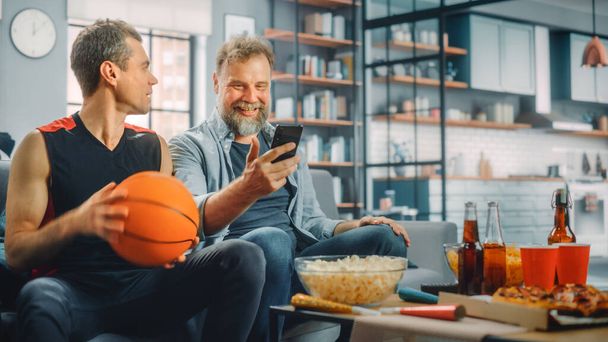 At Home Two Fans on Couch Watch Basketball Game on TV, Use Smartphone App for Checking Score, Online Bet, Statistics, Celebrate Team Win Championship. Friends Watch Favourite Club Play - Fotografie, Obrázek