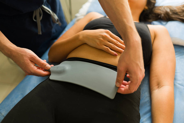 Gros plan d'une jeune femme qui reçoit un traitement contre l'hyperthermie à l'abdomen alors qu'elle parle à son médecin à la clinique - Photo, image