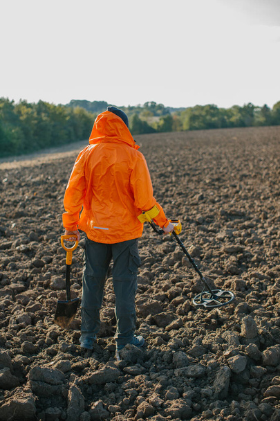 Egy fiatalember kincset keres egy fémdetektorral egy szántott mezőn.. - Fotó, kép