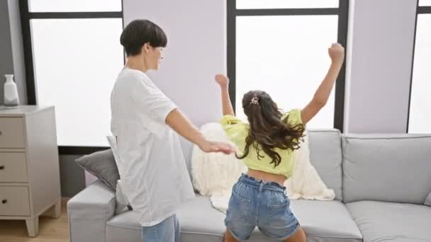Vreugdevolle moeder en dochter dansen vol vertrouwen samen, stralen geluk uit in de woonkamer van hun huis, terwijl ze luisteren naar een vrolijk lied. - Video