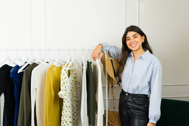 Fröhliche junge Frau aus Lateinamerika blättert durch Kleider in einer modischen Boutique - Foto, Bild