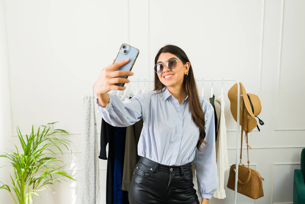 Giovane donna alla moda in abito elegante scatta un selfie con smartphone in un moderno negozio di abbigliamento - Foto, immagini