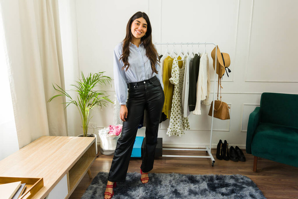 glimlachende jonge vrouwelijke ondernemer staat trots in haar goed versierde kleding boetiek thuis - Foto, afbeelding