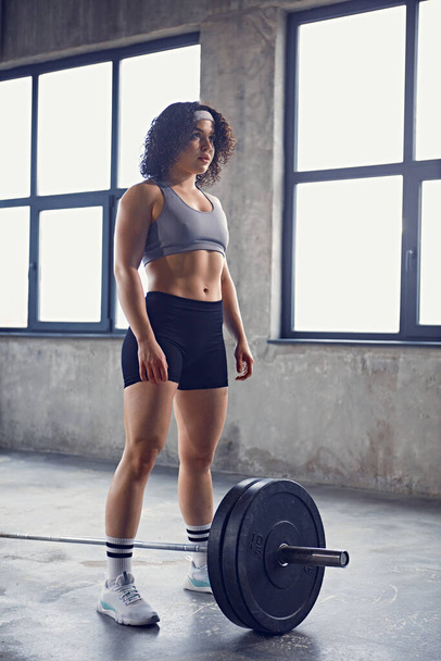 Full-length portrait of young athletic woman dressed sportswear stands preparing to lifting training with barbell. Concept of professional sport, active lifestyle, bodybuilding. Ad - Foto, afbeelding