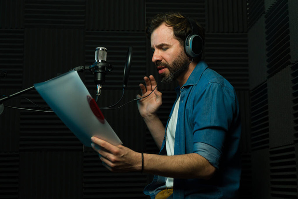 Αντρας ηθοποιός φωνής με ακουστικά εκτελεί σε στούντιο ηχογράφησης με ηχομόνωση - Φωτογραφία, εικόνα
