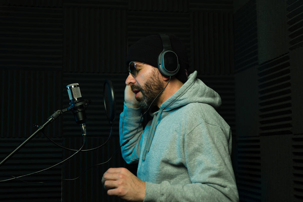 Konzentrierter männlicher Tonproduzent mit Kopfhörer nimmt Gesang in einem schalldichten Tonstudio auf - Foto, Bild