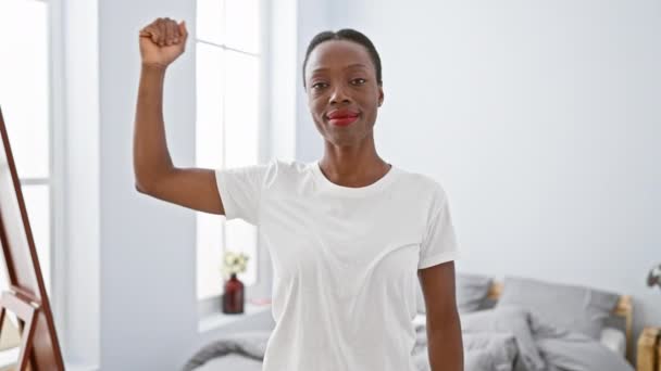 Fuerte mujer afroamericana flexionando el músculo del brazo en el dormitorio, viviendo un estilo de vida saludable en casa, orgullosa de su poder y condición física - Imágenes, Vídeo