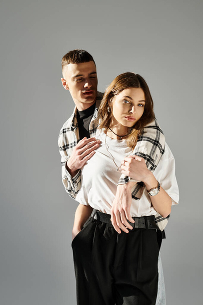 Ένας νεαρός άνδρας και μια γυναίκα ποζάρουν μαζί σε ένα στούντιο σε ένα γκρίζο φόντο, αποπνέοντας αγάπη και οικειότητα.. - Φωτογραφία, εικόνα
