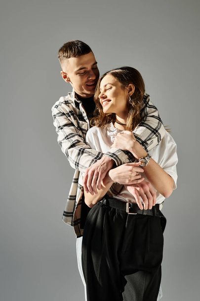 Ένας άντρας κρατά τρυφερά μια γυναίκα στην αγκαλιά του, δείχνοντας αγάπη και στοργή σε ένα στούντιο πάνω σε ένα γκρίζο φόντο.. - Φωτογραφία, εικόνα