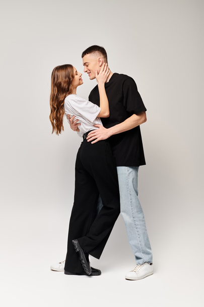 Un joven hombre y una mujer de pie juntos, expresando amor y conexión en un estudio con un fondo gris. - Foto, Imagen