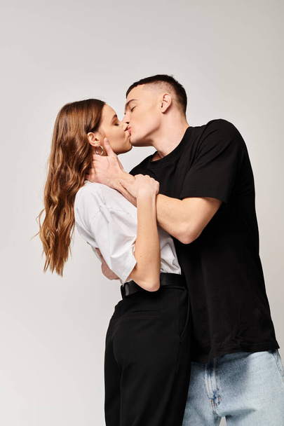 Молодий чоловік і жінка поділяють палкий поцілунок в студії з сірим фоном. - Фото, зображення