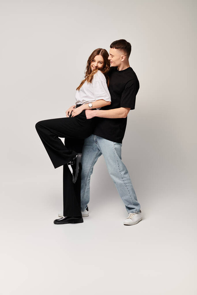 Un homme tient tendrement une femme dans ses bras, exprimant amour et affection dans un studio avec un fond gris. - Photo, image