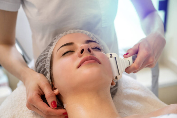 zbliżenie się młoda kobieta otrzymywać elektryczny ultrusound masaż twarzy w salon piękności - Zdjęcie, obraz