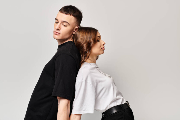 Mladý zamilovaný pár, stojící bok po boku ve studiu s šedým pozadím, vyzařující spojení a jednotu. - Fotografie, Obrázek