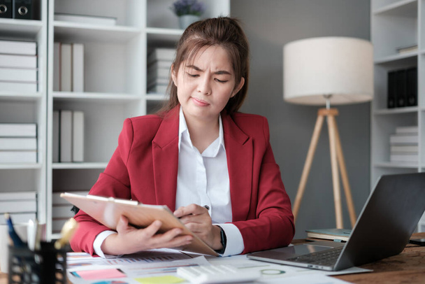 Femme d'affaires asiatique stressée travaillant sur ordinateur portable et calculant avec calculatrice financière à partir de statistiques graphiques de données, graphiques. Des résultats d'affaires réussis dans le bureau moderne portent une chemise rouge. Haut - Photo, image