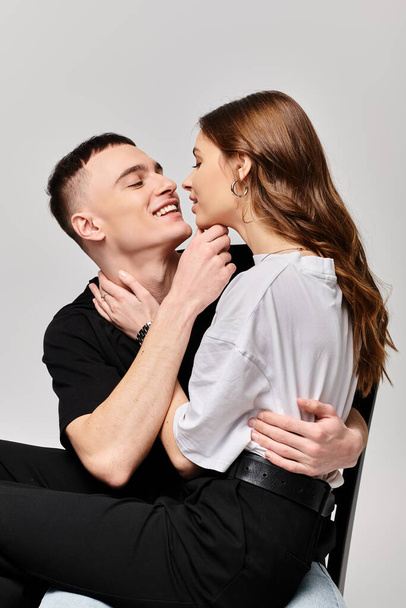 A young man and woman sit closely together on a chair in a studio setting against a grey background. - Photo, Image
