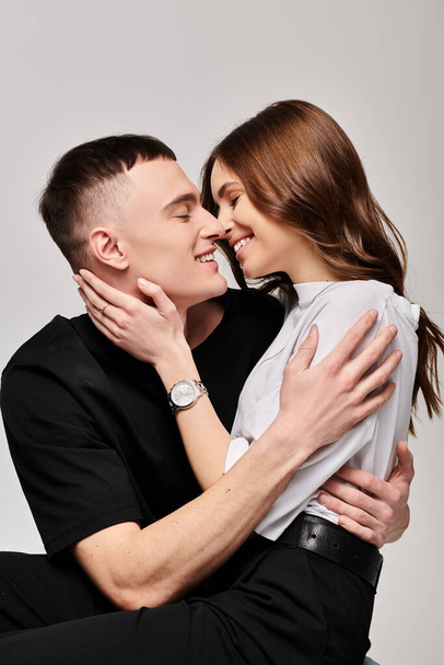 Een man en een vrouw knuffelen elkaar liefdevol in een studio met een grijze achtergrond. - Foto, afbeelding