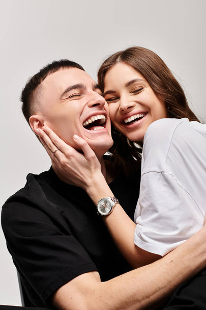 Nuori mies ja nainen syleilevät toisiaan rakastavasti, jakaen hellän halauksen harmaata studiotaustaa vasten. - Valokuva, kuva