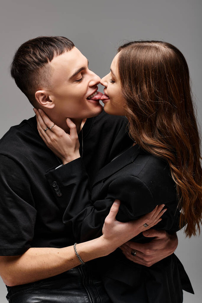 Ένας νεαρός άνδρας και μια γυναίκα κλειδώνουν τα χείλη σε ένα παθιασμένο φιλί σε ένα γκρίζο φόντο στούντιο. - Φωτογραφία, εικόνα