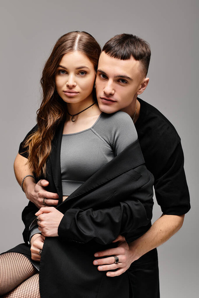 Un joven hombre y una mujer posan juntos en un estudio con un fondo gris, exudando amor y estilo. - Foto, Imagen