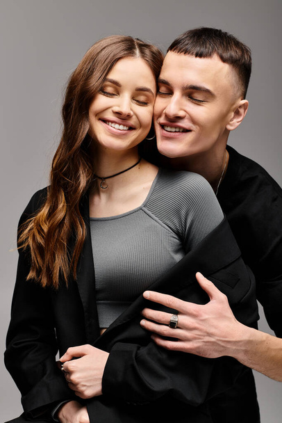 Een jonge man en vrouw omhelzen elkaar liefdevol in een studio met een grijze achtergrond. - Foto, afbeelding
