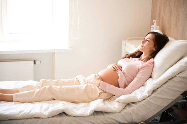 Belle patiente se couche sur le lit dans la salle d'hôpital avant l'accouchement - Photo, image