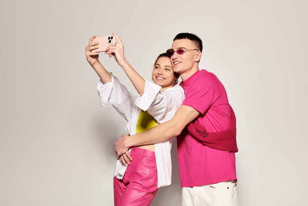 Ein stylisches junges verliebtes Paar macht gemeinsam ein Selfie in einem Studio mit grauem Hintergrund. - Foto, Bild