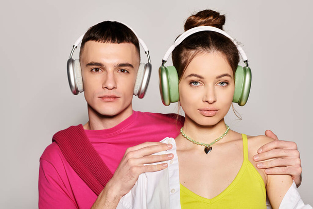 Stylowa młoda para zakochana w sobie słuchawki, zanurzone w muzyce z szarym tle studio. - Zdjęcie, obraz