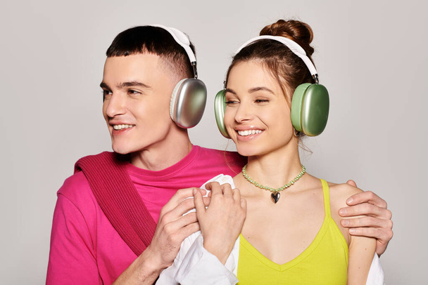 Стильная молодая влюбленная пара, слушающая музыку в наушниках в студии на сером фоне. - Фото, изображение