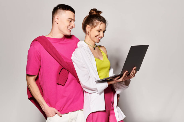 Um jovem casal elegante apaixonado, focado e engajado enquanto olham para uma tela de laptop juntos em um estúdio com um fundo cinza. - Foto, Imagem