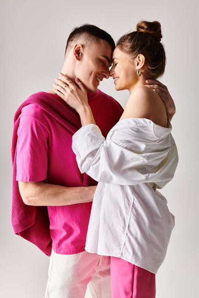 Un homme et une femme, élégamment vêtus, se tiennent côte à côte dans un studio sur un fond gris, se regardant avec amour. - Photo, image