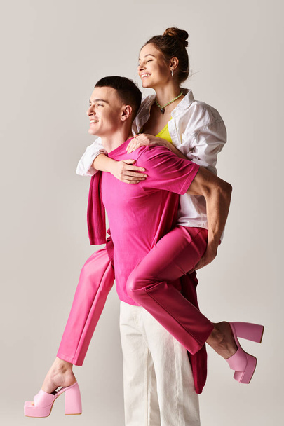 Um homem e uma mulher, vestidos de rosa, posam juntos em um estúdio com um fundo cinza, mostrando seu amor e estilo. - Foto, Imagem