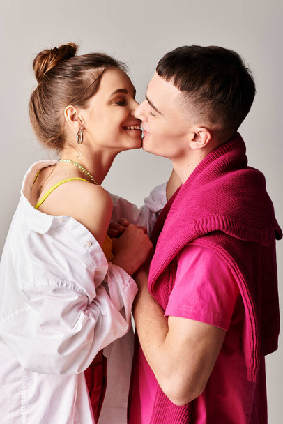 Ένας κομψός νέος και μια γυναίκα μοιράζονται ένα παθιασμένο φιλί σε ένα στούντιο σε ένα γκρίζο φόντο. - Φωτογραφία, εικόνα