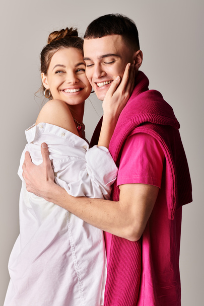 Un jeune couple élégant amoureux, se serrant dans ses bras avec une véritable affection, debout sur un fond de studio gris. - Photo, image