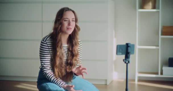Красива молода жінка, яка впливає на онлайн трансляцію через смартфон на тринозі у вітальні вдома - Кадри, відео