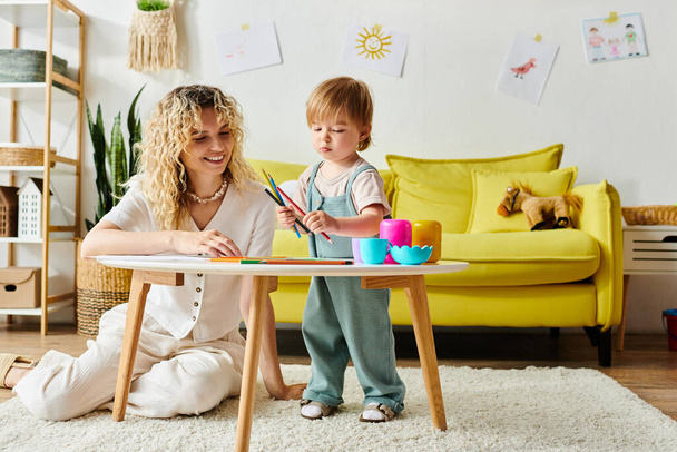 Eine lockige Mutter und ihre kleine Tochter sitzen an einem Tisch und unternehmen zu Hause gemeinsam Montessori-Lernaktivitäten. - Foto, Bild