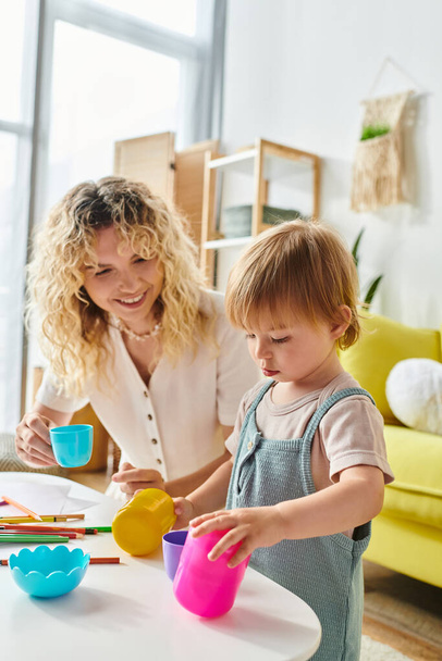 Kręcone matka i jej córka maluch angażują się w zabawy Montessori Cup działalności w domu. - Zdjęcie, obraz