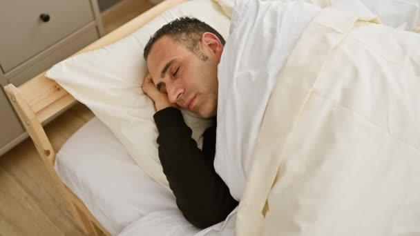 Ein junger hispanischer Mann schläft friedlich in einem hell erleuchteten Schlafzimmer und stellt Ruhe und Entspannung zu Hause dar. - Filmmaterial, Video