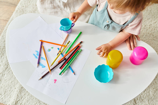 Ένα μικρό κορίτσι παίζει με χαρά με χρωματιστές κραγιόνια σε ένα τραπέζι ως μέρος μιας εκπαιδευτικής δραστηριότητας Montessori στο σπίτι. - Φωτογραφία, εικόνα