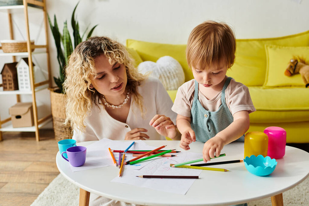 A curly mother and her toddler daughter sit at a table using crayons for Montessori education. - Photo, Image