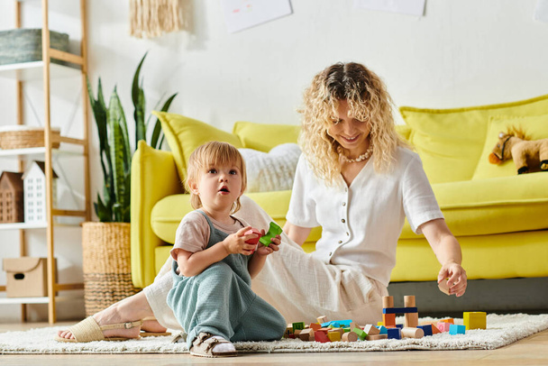 Σγουρή μητέρα και η κόρη του μικρού παιδιού συμμετέχουν σε παιχνιδιάρικο Montessori μέθοδος εκπαίδευσης στο σπίτι, κάθεται στο πάτωμα. - Φωτογραφία, εικόνα